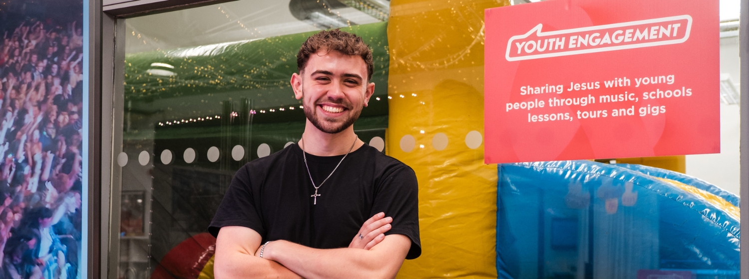 Staff member smiling in front of a sign saying 'youth engagement'