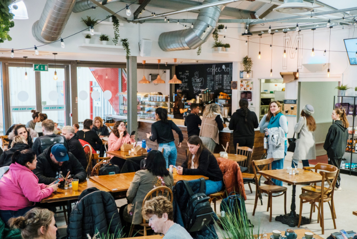 The Mess Cafe is busy with people sitting at the tables and others queuing for coffee.