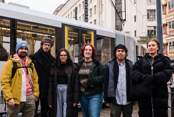 A group of students hang out in the city centre with a tram passing by.