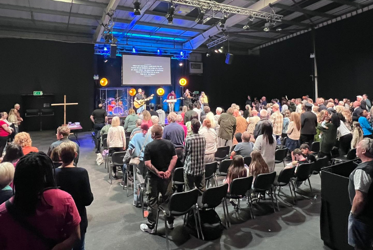 A Sunday service at Message Community Church, a room full of people singing and a band on the stage.