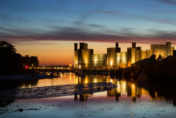 Caernarfon Castle at night reflected in the water.
