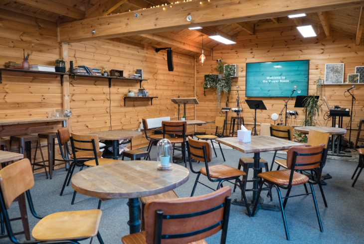 Prayer cabin with small tables and chairs, book shelves and TV on the wall.