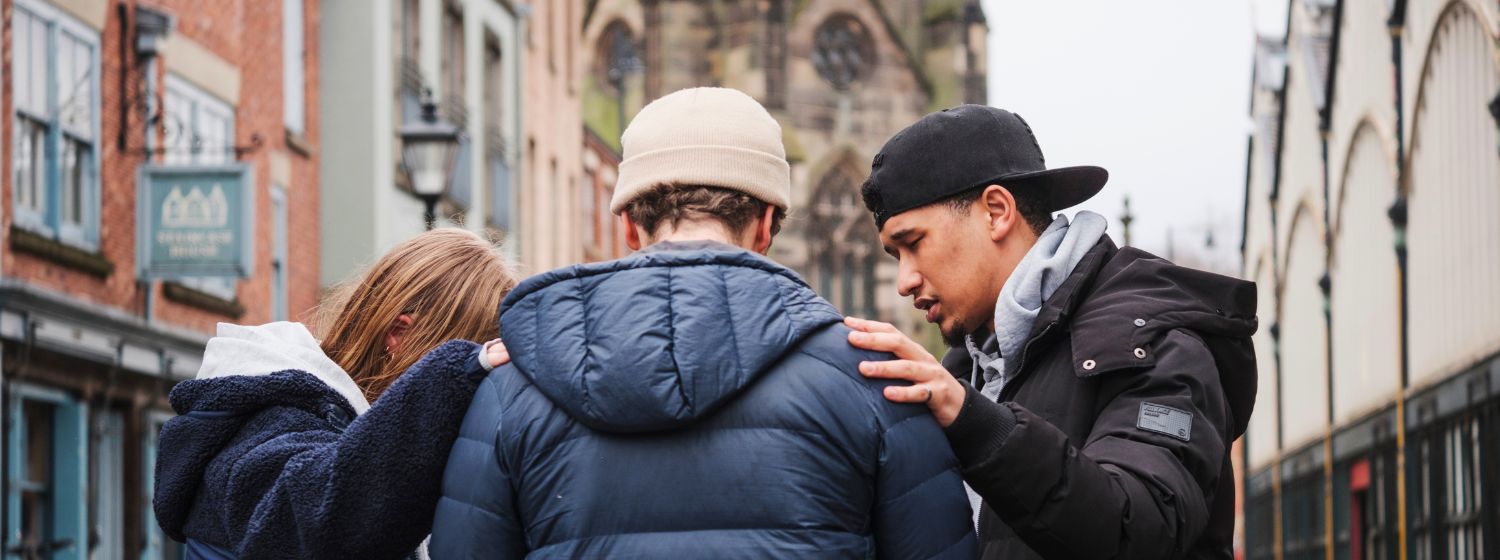 Two MSE students pray with a man in the street.