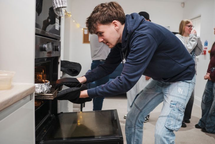A student takes something out of the oven in the student accommodation kitchen.