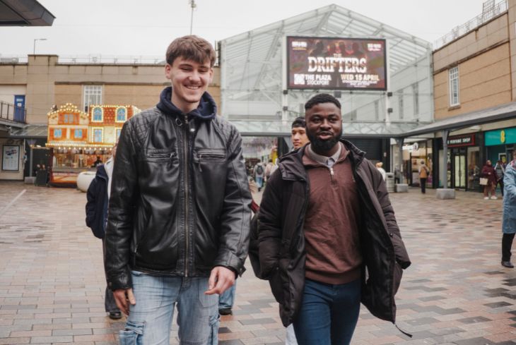 Two students walk through the town centre wearing winter jackets.
