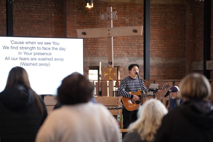 A man leads worship on a guitar at the front of church.
