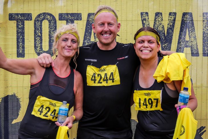 Three people celebrate at the finish line of an obstacle course fundraiser.
